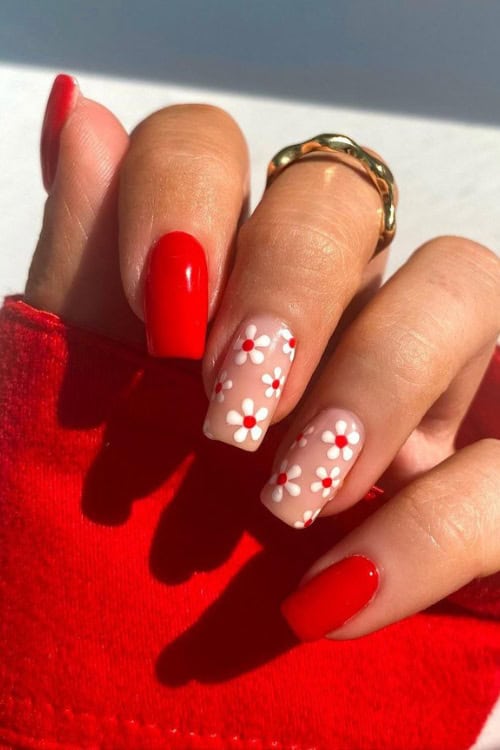 Red nails with white floral accent on ring finger.