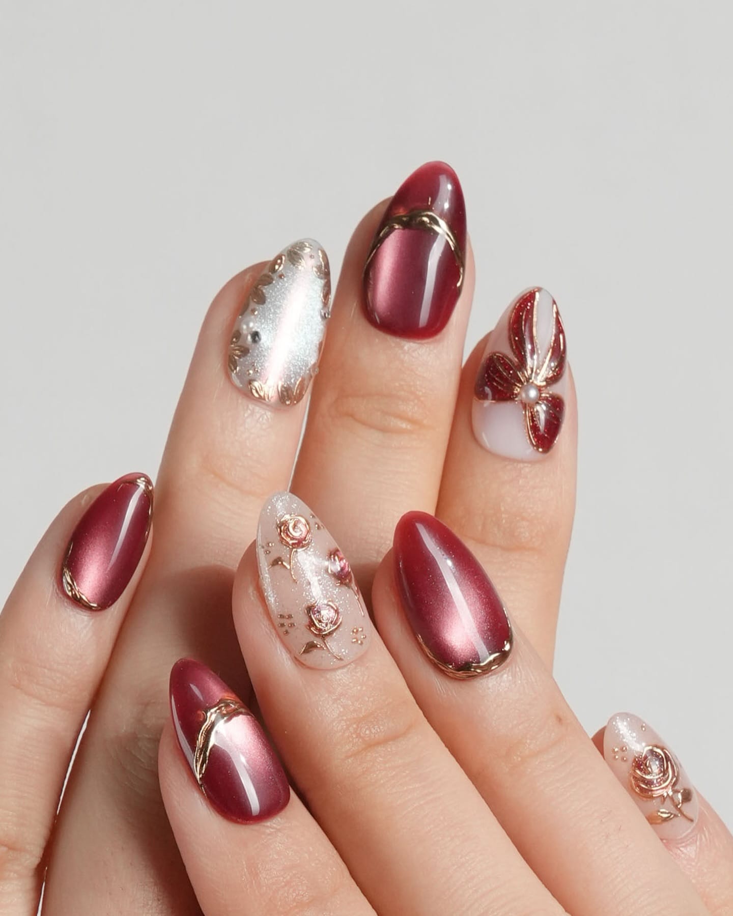 Maroon nails with gold and silver embellishments, opulent and detailed.
