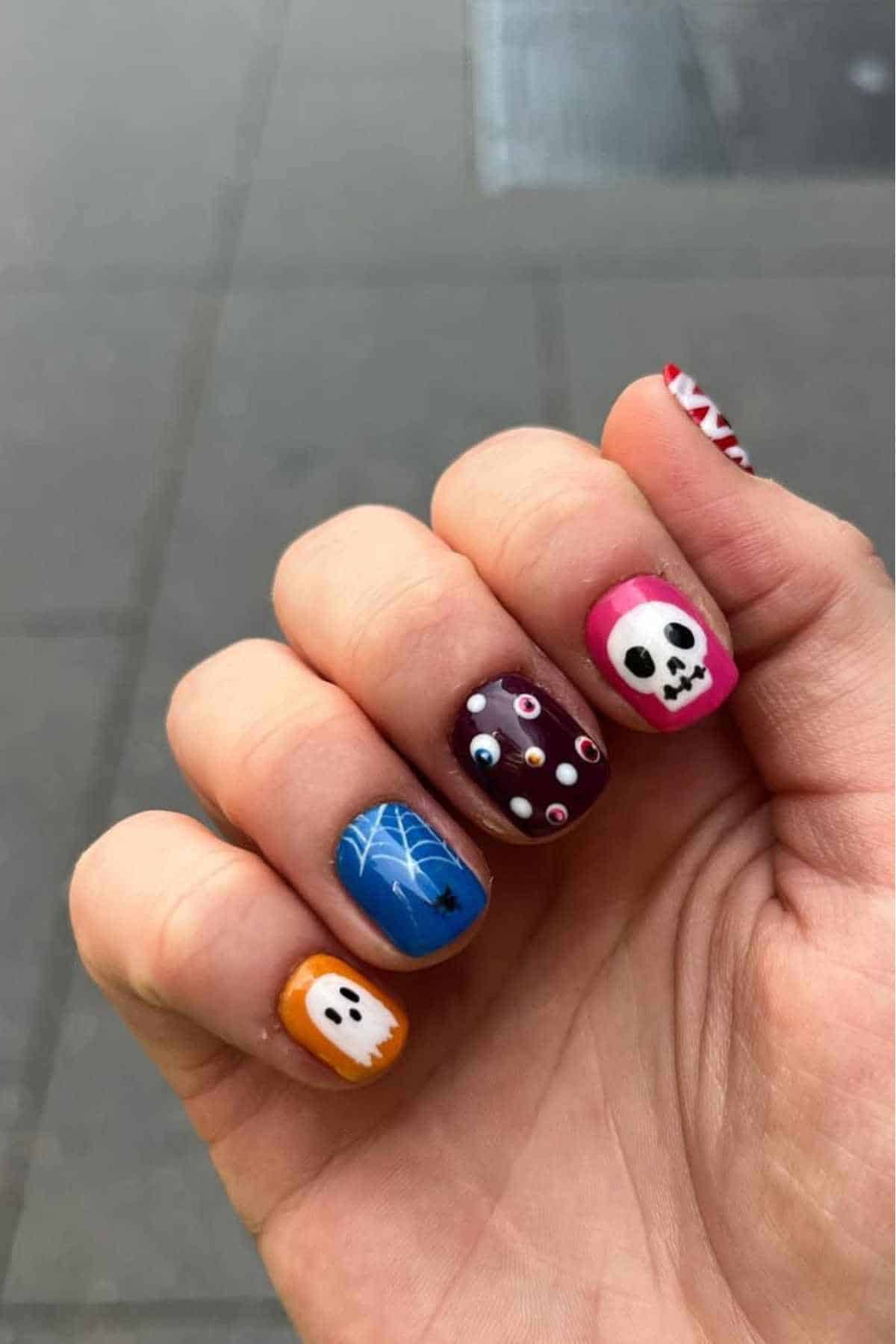 Colorful Halloween-themed nail art with skulls and webs