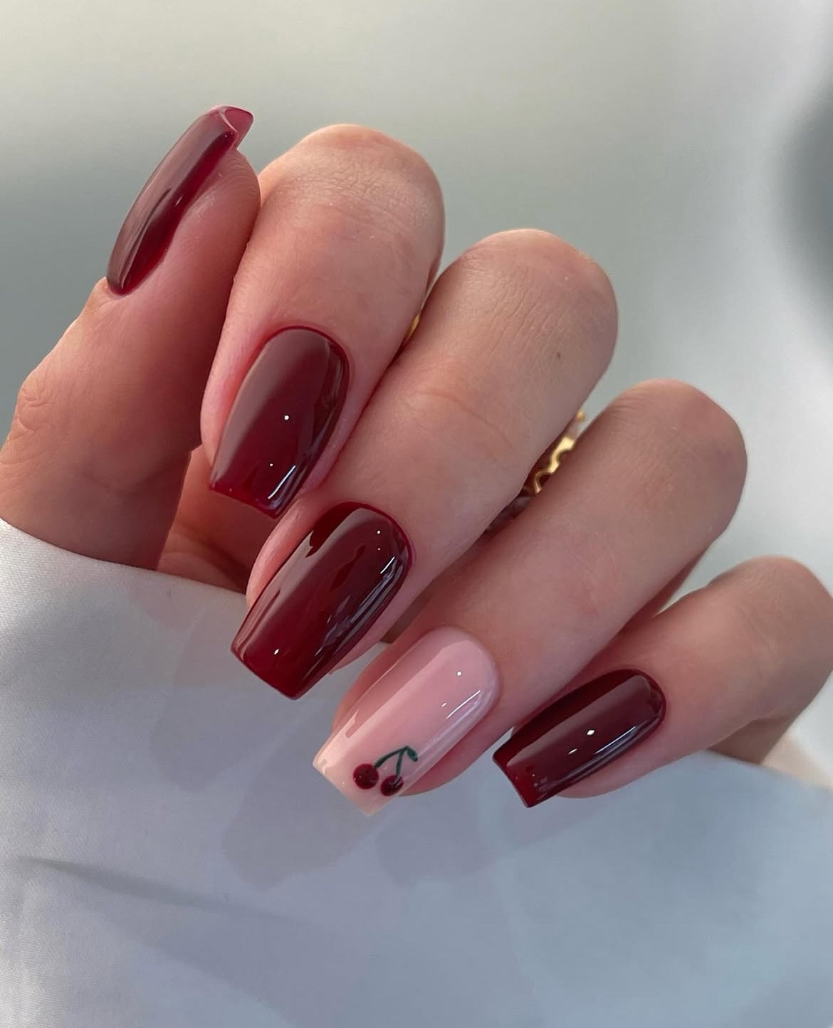 Square nails with burgundy polish and cherry accent