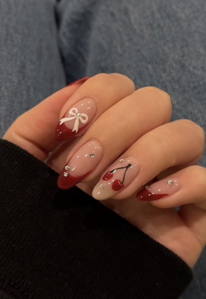 Almond nails with red tips, white bow, and cherry art