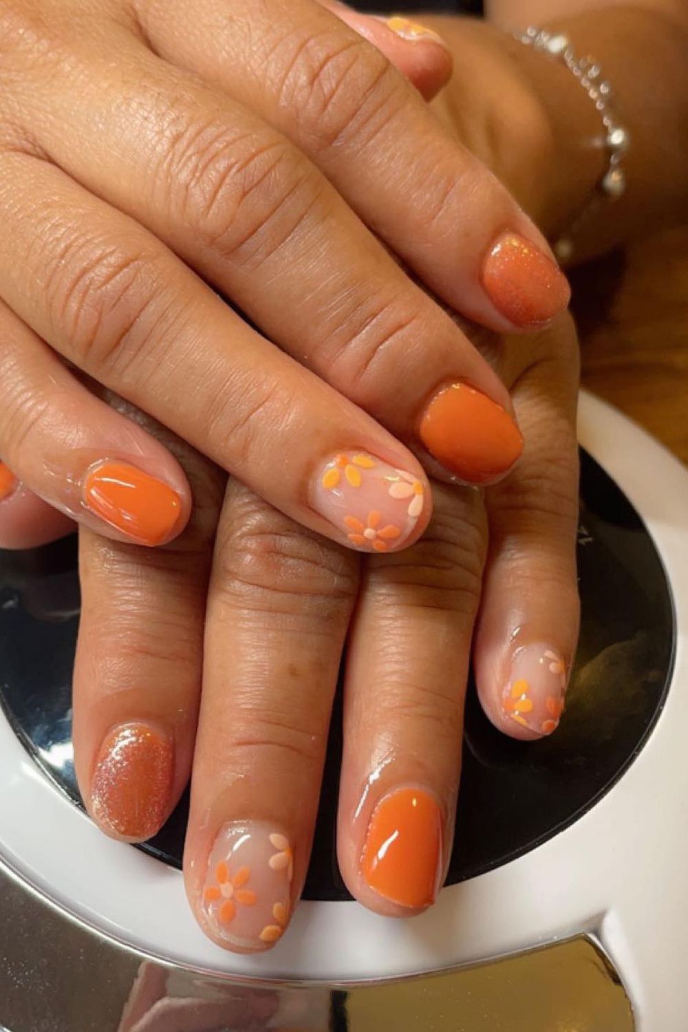 Orange floral nail art on short round nails.