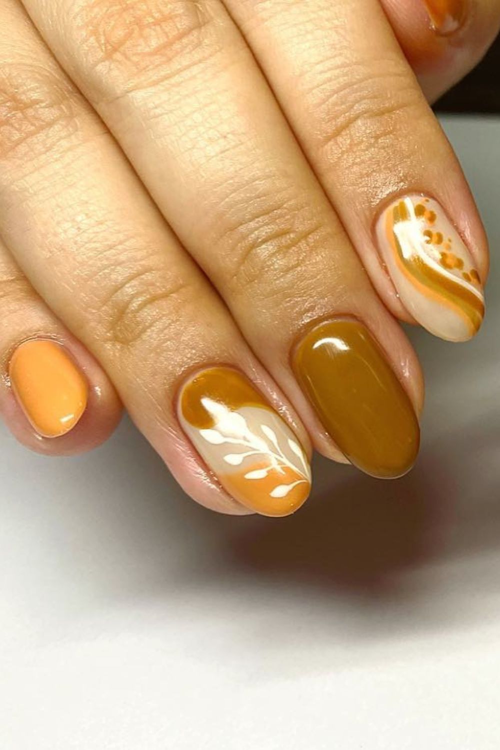 Earthy tones with leaf art on medium nails.