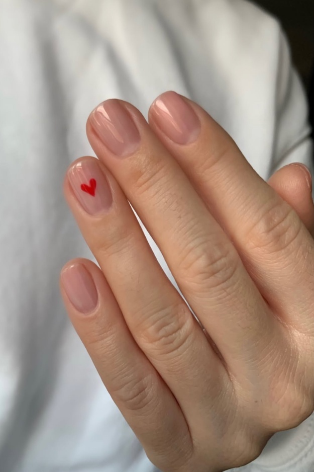 Nude square nails with tiny red heart accent, ideal for minimal and romantic styles.